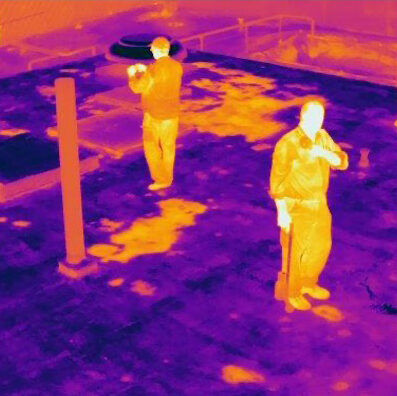 An infrared roof survey in progress, with an infrared camera mounted on a tripod and pointed at a commercial roof.
